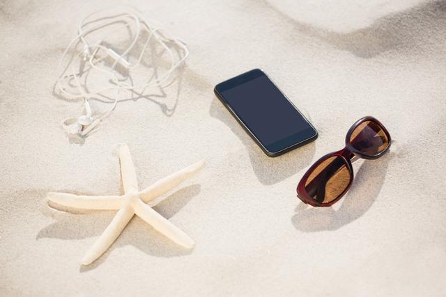 Starfish, sunglasses, headphones and mobile phone kept on sand at beach