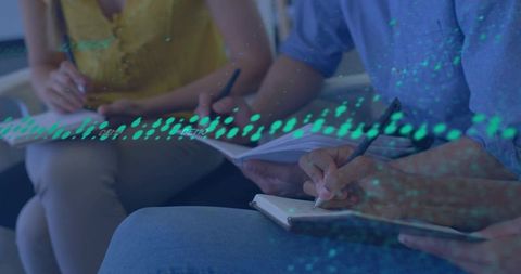 Group writing in workshop with notebooks on lap teal-blue data overlay collaborative learning