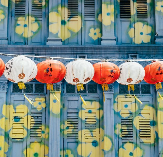 This image depicts a row of red and white Chinese lanterns hanging against a graffiti-covered wall. The wall features yellow flower graffiti designs, adding a vibrant contrast to the traditional lanterns. Useful for themes of cultural festivals, urban art, decorations, and lifestyle articles focused on diverse cultural settings.