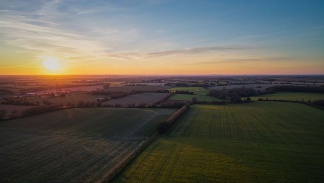 Aerial sunset over quilted farmland with hedgerows and patchwork agricultural fields