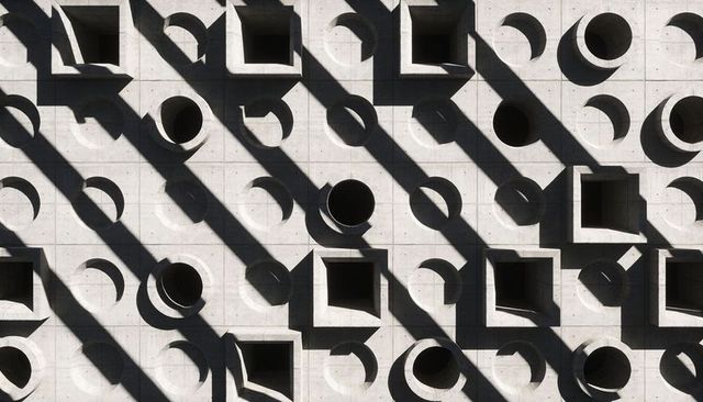 Brutalist concrete facade featuring round and square apertures with diagonal shadows
