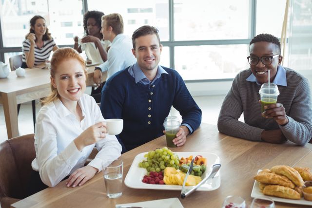 High angle portrait of smiling business colleagues sitting at breakfast table in office cafeteria
