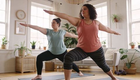 Curvy Women Practicing Home Yoga Warrior Pose in Sunlit Living Room for Wellness and Balance