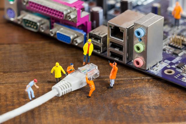 Miniature engineers and workers are connecting a LAN cable to a computer, symbolizing teamwork and technology. This creative and conceptual image can be used for illustrating IT services, network maintenance, technology blogs, and educational materials about computer networking.