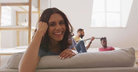 Smiling woman relaxing at home with friends playing guitar