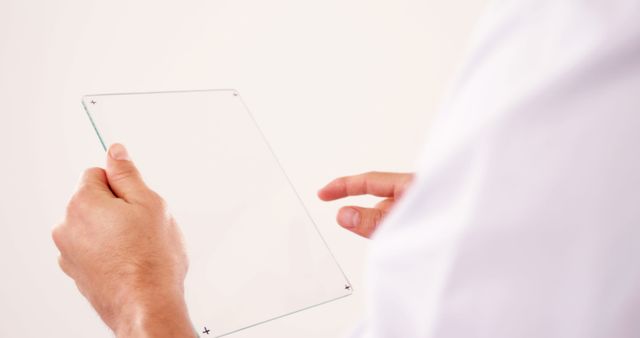 A pair of hands holding a clear, transparent glass tablet, against a white background. The modern, minimalist design emphasizes innovation and futuristic technology. Useful for tech and innovation related promotions, digital transformation concepts, and presentations emphasizing minimalism and cleanliness.