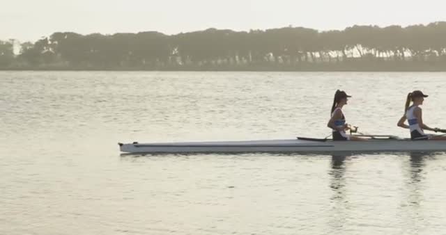 This stock photo captures four young Caucasian women rowing together in a racing shell on a river during sunrise. The scene emphasizes teamwork, strength, and fitness. Ideal for use in content promoting outdoor activities, team sports, women empowerment, or healthy lifestyles. Perfect for articles, blog posts, or advertisements aimed at showcasing women in sports and teamwork exercises.