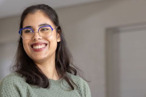 Smiling woman wearing blue-rimmed glasses and green knit sweater looking right