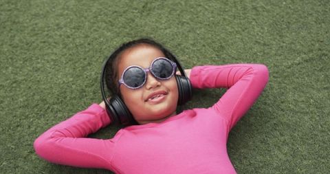 Smiling Child Relaxing with Sunglasses and Headphones on Green Grass