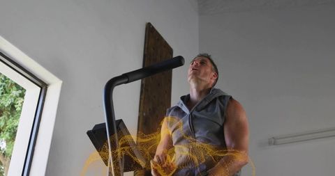 Mid-adult man pedaling elliptical trainer in minimalist home gym wearing sleeveless hoodie