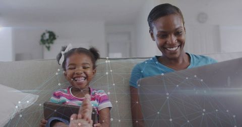 Mother and daughter laughing while using tablet and laptop with network overlay