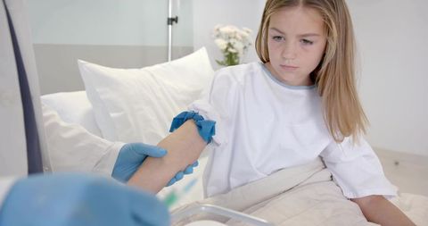 Young girl receiving blood draw while nurse applying tourniquet in pediatric clinic