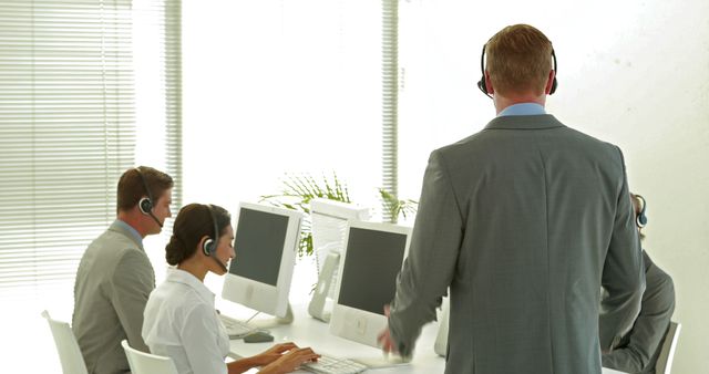 Professionals wearing headsets working on computers in a modern, bright office space. Ideal for illustrating teamwork, customer service environments, professional office settings, and collaborative workspaces.