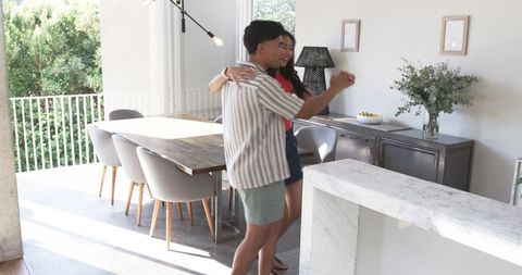 Asian couple embracing near marble kitchen island in sunlit modern open-plan dining room