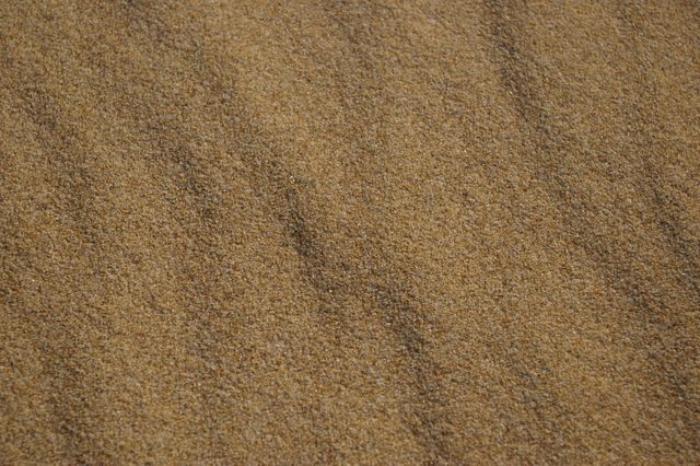 Close-up view of fine sand texture showcases the individual grains and natural patterns. Perfect for use in backgrounds, websites, presentations about natural elements, environmental topics, and design projects requiring a neutral and earthy feel.