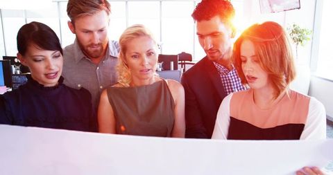 Collaborative team reviewing blueprint planning project strategy in bright modern office