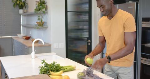 African American man arranging apples and herbs on marble kitchen island in modern minimalist kitche