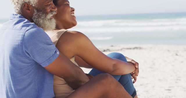 Happy african american couple sitting and embracing on sunny beach - Download Free Stock Photos Pikwizard.com