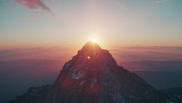 Sunrise over jagged mountain peak with lens flare