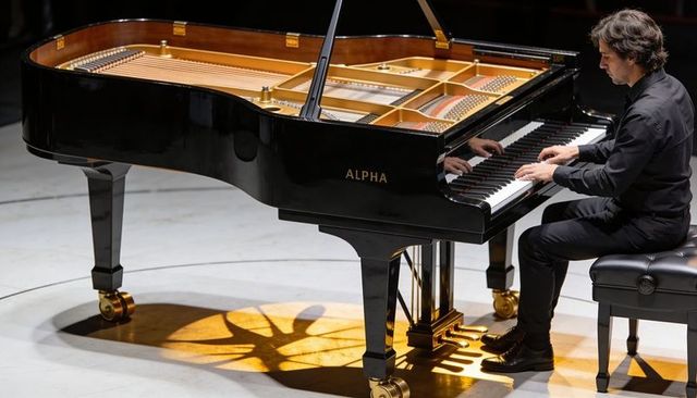 Pianist playing alpha grand piano under spotlight revealing strings and pedals