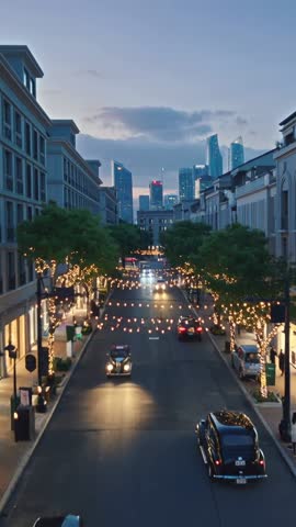 Vertical twilight shopping street video of man walking under string lights as vintage cars pass