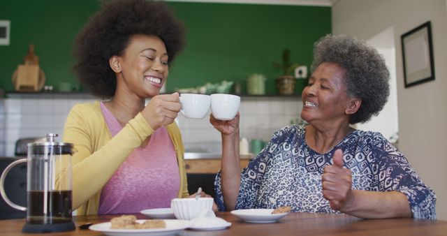 An elderly woman and a young woman are enjoying a special moment together in the kitchen, sharing coffee and cookies while smiling warmly. Perfect for promoting family bonding, generational relationships, cozy home environments, and the joy of spending time with loved ones.