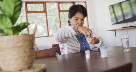 Senior indian woman organizing medication at home dining table with pill bottles and plant