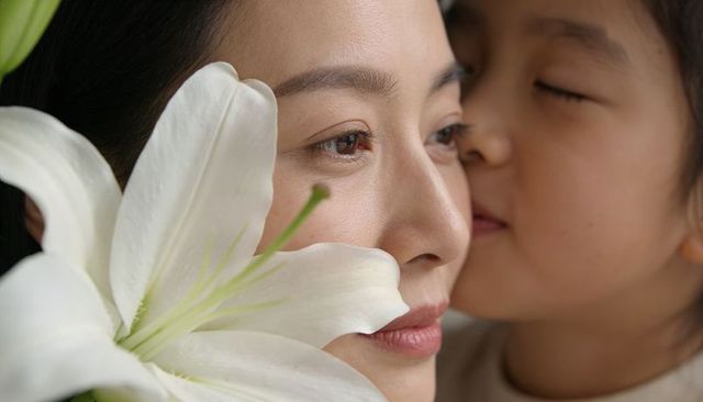 Nuzzling asian mother and daughter sharing tender moment with large white lily closeup