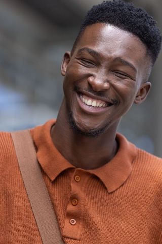 Laughing african man wearing rust knit polo and shoulder bag, urban portrait headshot