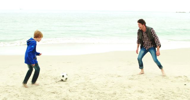 Father and son enjoying a sunny day playing soccer on the beach. This image can be used to promote family activities, outdoor sports, summer vacations, and concepts of bonding and happiness in advertisements, blogs, and social media posts.