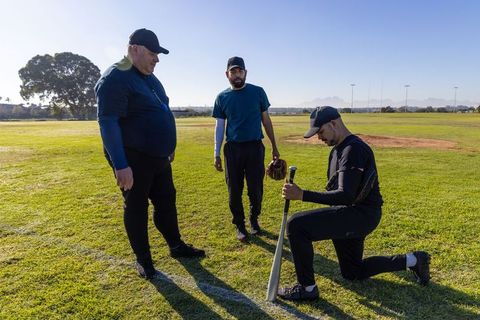 Baseball players preparing for practice on sunlit field with bat and glove