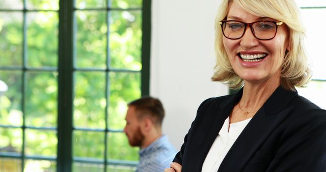 Confident Businesswoman Smiling in Office with Colleague in Background - Download Free Stock Images Pikwizard.com