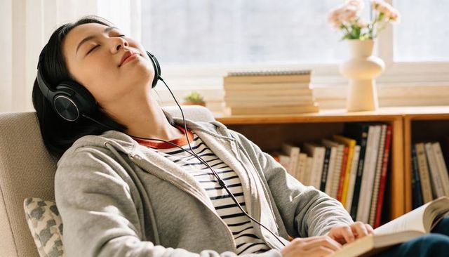 Sunlit cozy reading nook woman in hoodie relaxing with headphones and open book