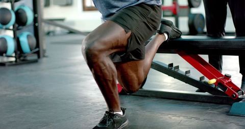 African american trainer spotting athlete performing bulgarian split squat on bench strength