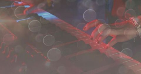 Playing synthesizer keyboard in concert lights, close-up right hand with bracelet