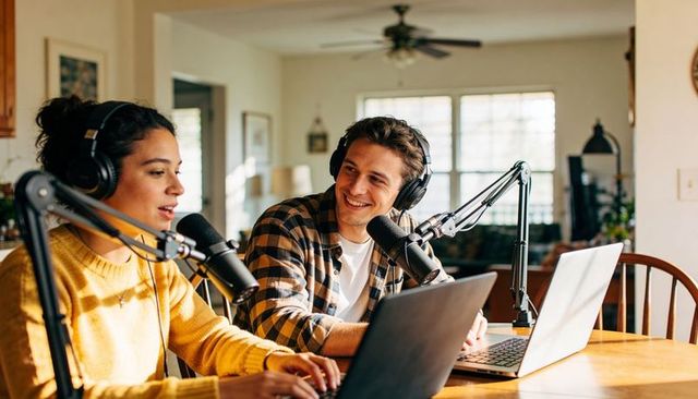 Young cohosts recording podcast at home studio with condenser mics and laptops