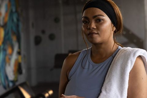Focused asian woman training in industrial gym with towel over shoulder