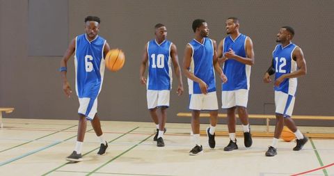 Young basketball players dribbling, walking and talking during indoor team practice session