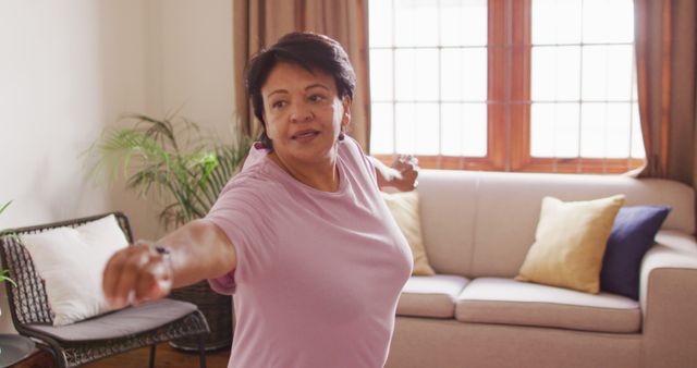 Senior woman practicing yoga in her living room, focusing on a stretching routine. This image can be used for promoting wellness and healthy lifestyle activities for older adults, highlighting home fitness routines and representing relaxation and balance exercises.