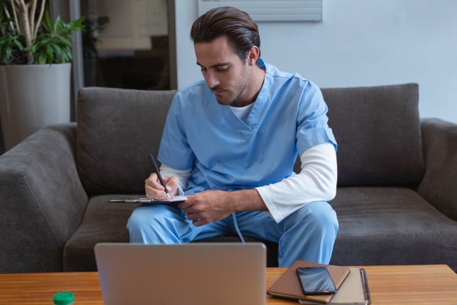 Front view of male surgeon writing on clipboard while sitting on sofa in lobby at hospital