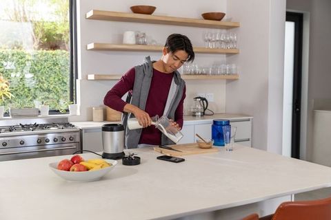 Pouring milk into blender on modern kitchen island, young asian man making smoothie