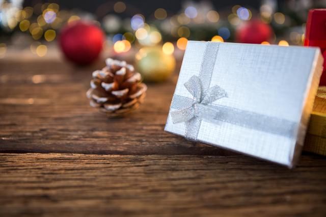 Christmas gifts wrapped in silver paper with a pine cone on a wooden table, surrounded by festive bokeh lights. Ideal for holiday greeting cards, festive advertisements, Christmas promotions, and seasonal blog posts.