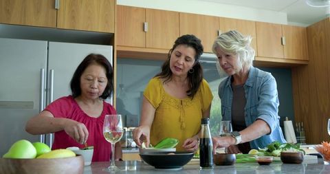 Diverse friends preparing healthy salad on kitchen island with wine glasses