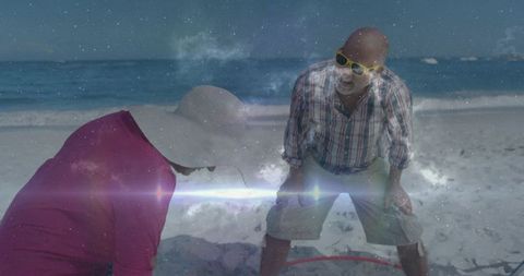Senior couple inspecting red hoop on sunny beach with lens flare and cosmic nebula overlay