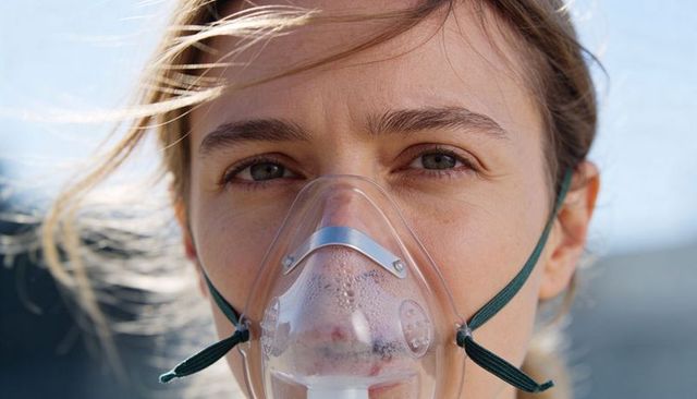 Young woman wearing oxygen mask outdoors with windblown hair and sunlit condensation
