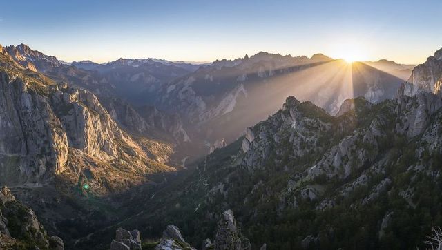 Sunburst Rising Over Jagged Alpine Peaks Casting Golden Rays Across Misty Valley