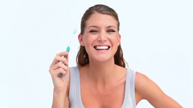 A woman happily brushing her teeth embodies effective personal hygiene habits against a white background, suggesting cleanliness and health. Suitable for dental care advertisements, hygiene brochures, or wellness blogs emphasizing oral health routines.