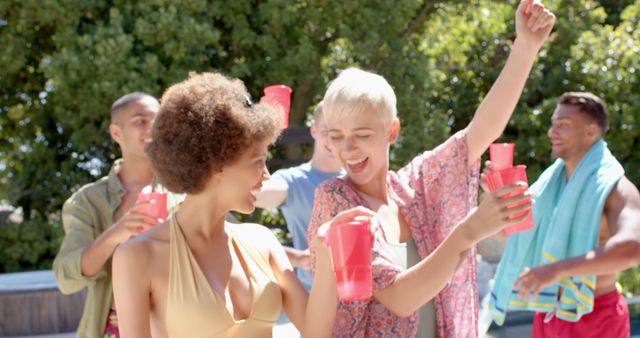 This photo shows young adults celebrating at an outdoor pool party with red cups, dancing and having fun in the sun. Ideal for advertisements and social media posts related to summer activities, youth parties, leisure activities, and social gatherings. Perfect for websites, blogs, and campaigns promoting a lively and festive atmosphere.