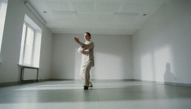 Woman practicing tai chi in minimal studio wearing beige tunic and wide trousers