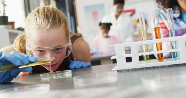 A girl is conducting a chemistry experiment in a school laboratory, wearing safety goggles and gloves. She is using a pipette to transfer liquid into a Petri dish. Background shows other students and laboratory equipment. Ideal for educational content, science and technology promotions, and STEM-related articles.